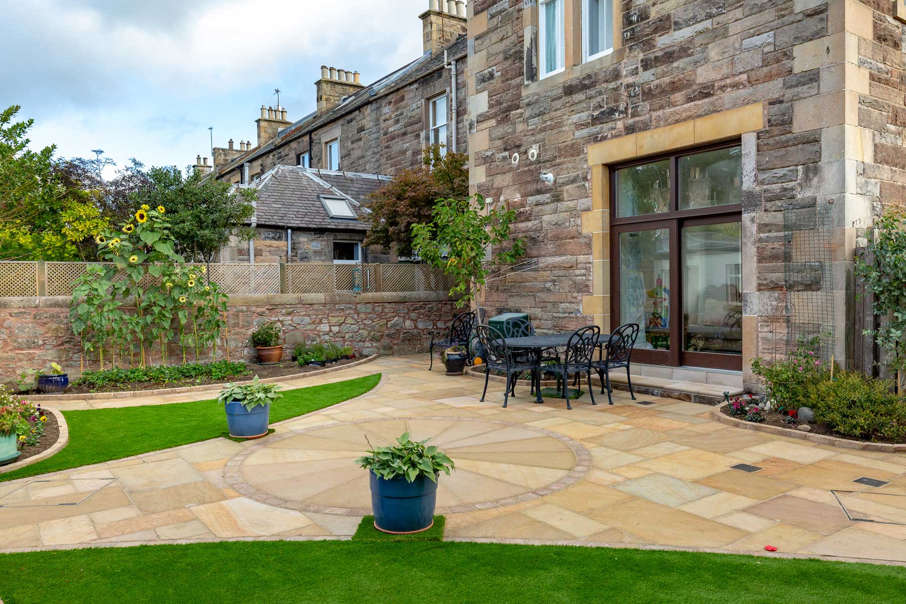Garden design, patio, paths, artificial grass & landscaping by Stow Construction & Landscaping in Morningside Grove, Edinburgh 2018 using Marshalls Fairstone Riven Harena Golden Sand, Marshalls Fairstone Riven Harena Golden Sand new circle, Marshalls Tegula Drivesett Harvest, Weatherpoint Buff 365, Marshalls Fairstone Sawn Vesuro bull-nosed step units, Namgrass, Marshalls Drivesett kerbs Harvest